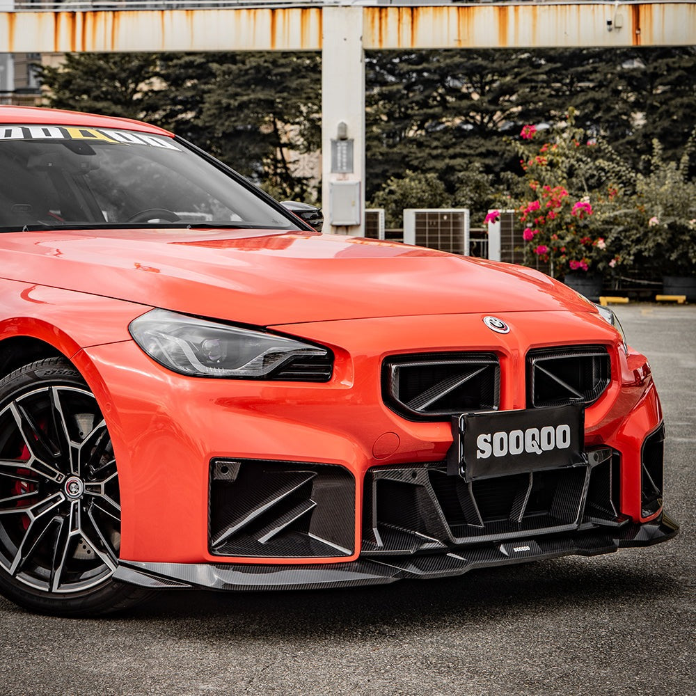 SOOQOO carbon fibre front ducts installed on BMW M2 (G87), front three-quarter view on orange car