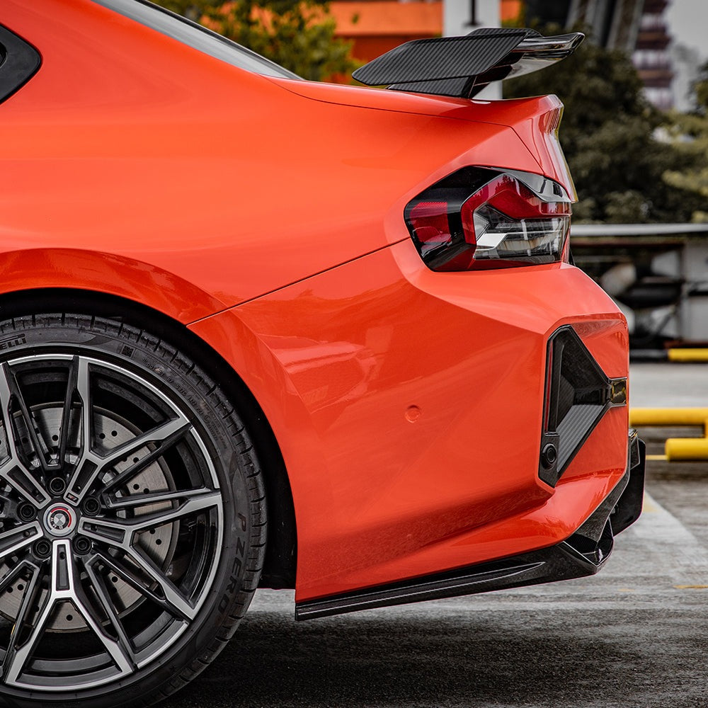 SOOQOO carbon fibre rear bumper inserts installed on BMW M2 (G87), rear quarter close-up on orange car