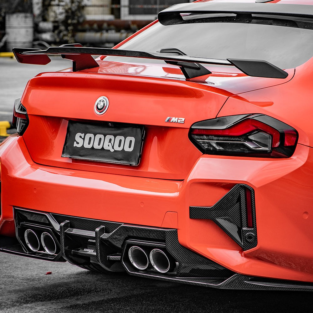 SOOQOO carbon fibre rear bumper inserts installed on BMW M2 (G87), rear three-quarter view on orange car